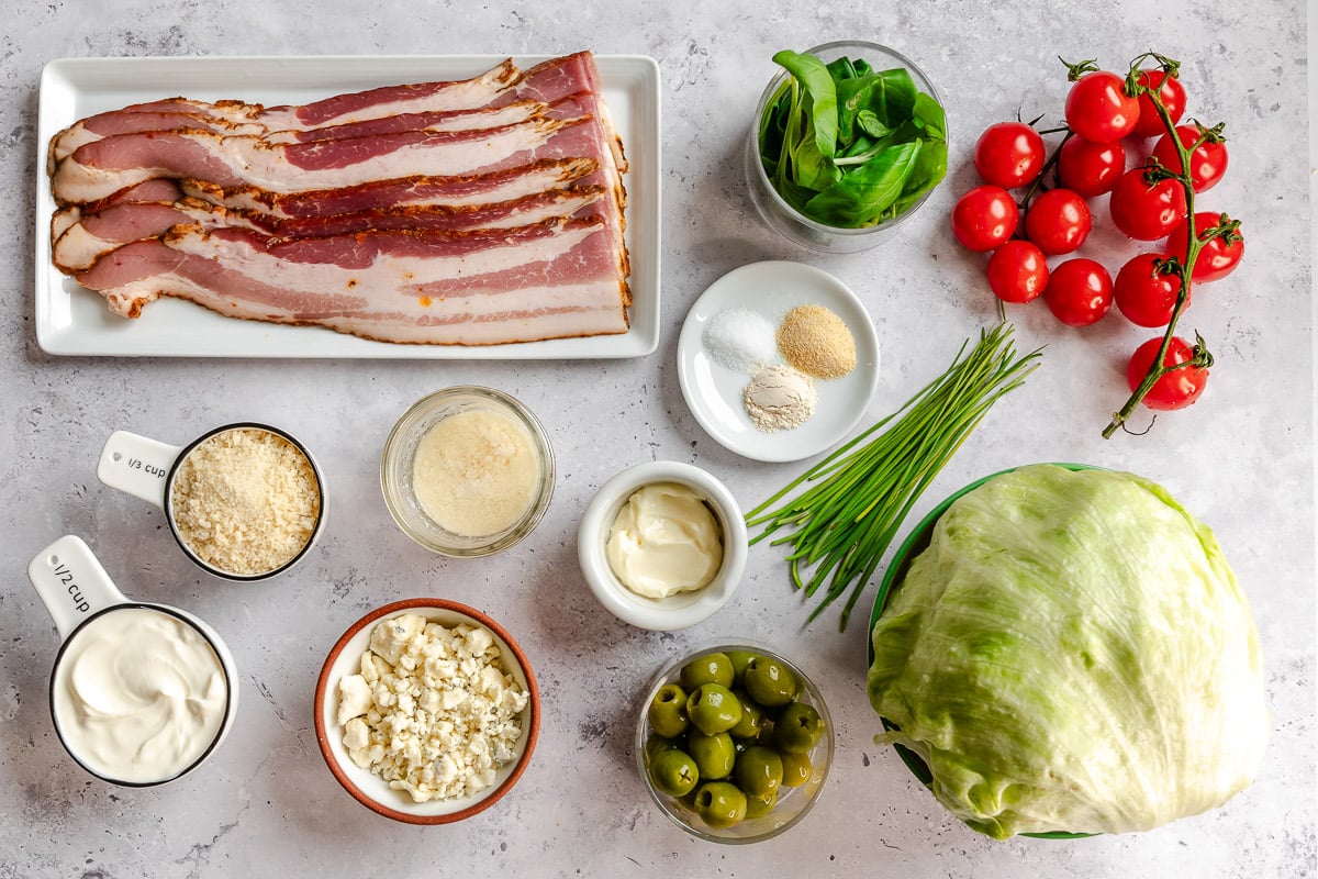 Assorted salad ingredients: bacon, lettuce, tomatoes, olives, cheese, mayonnaise, basil, chives, and seasonings.