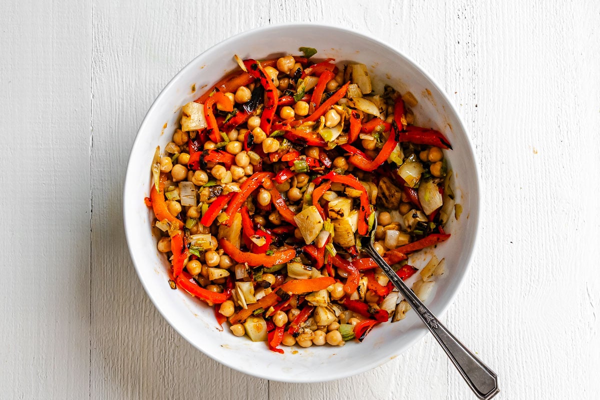 Chickpeas, sliced grilled bell pepper, diced grilled fennel, and minced grilled scallions all tossed together in a large white bowl.