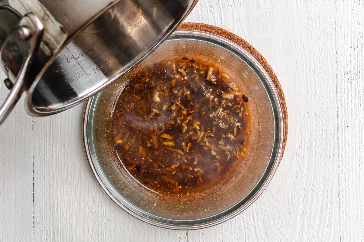 Hot oil being poured over spices and garlic in a glass bowl.