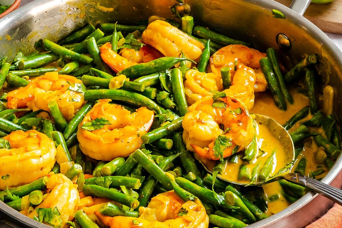 Shrimp and green beans in a yellow curry sauce, served in a skillet with a spoon.