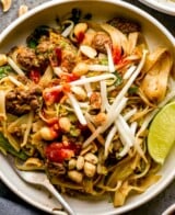 A bowl of ground beef pad thai topped with peanuts, bean sprouts, and lime wedges, with a fork on the side.