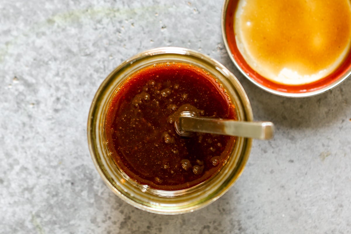 Pad Thai sauce in a glass jar with a spoon in it and the lid set nearby.
