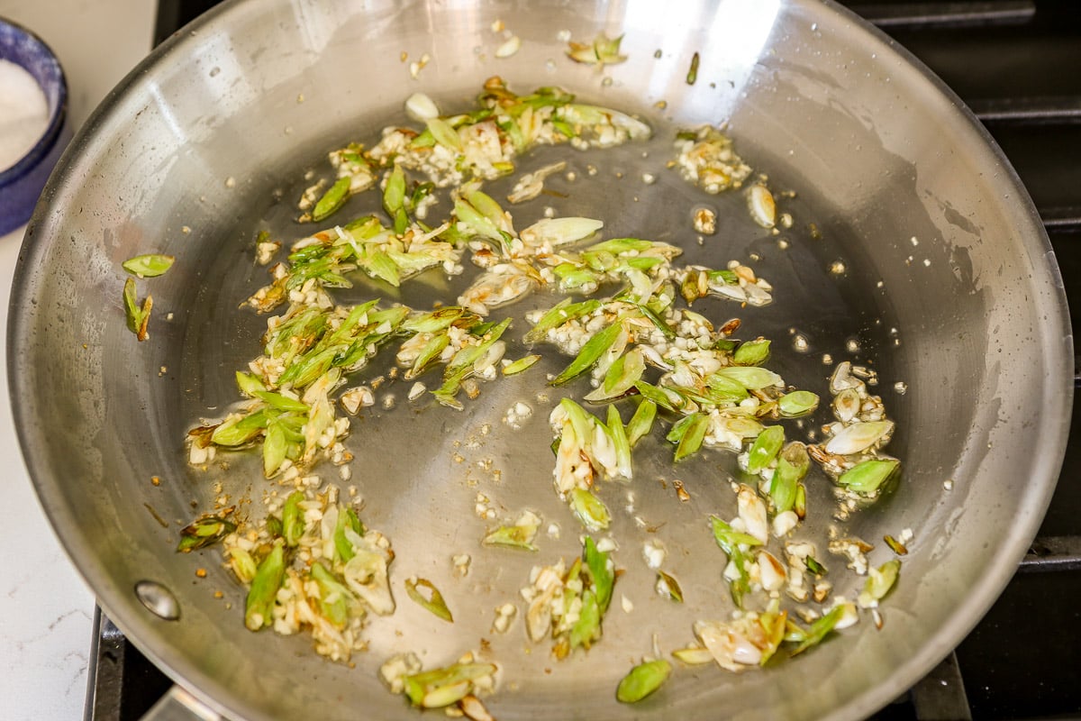 Sliced scallions and chopped garlic sauteeing in a large stainless steel skillet.