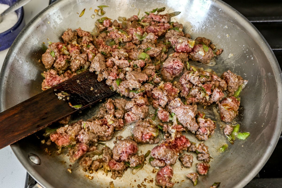 Ground beef cooking in a large stainless steel skillet.