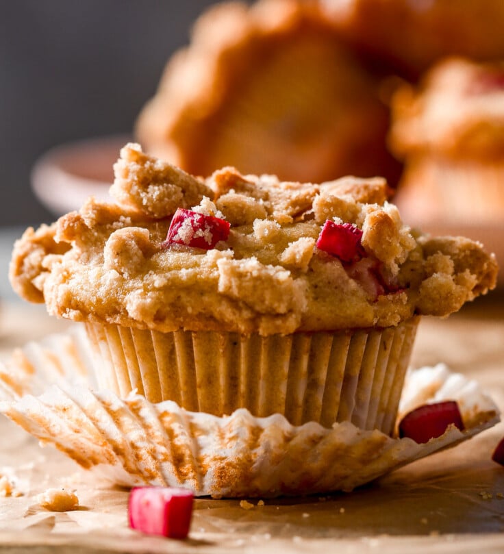 A close-up of a crumb-topped rhubarb muffin sitting on parchment paper with the wrapper peeled back.