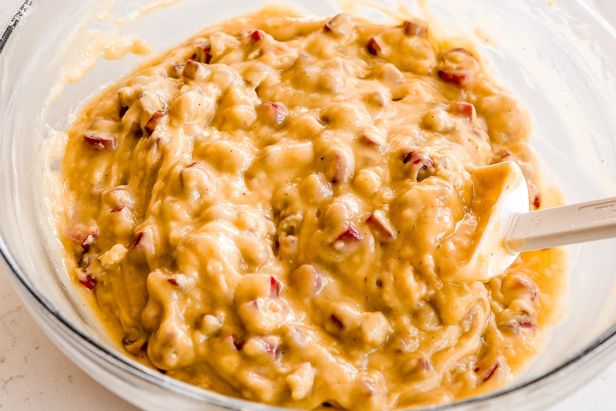 Muffin batter with diced rhubarb mixed in, in a large glass mixing bowl with a white rubber spatula set in it.