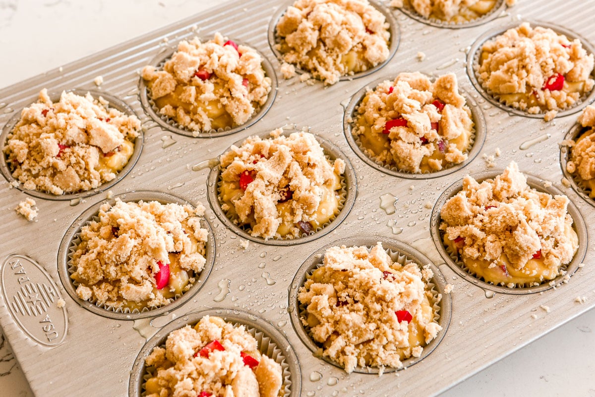 Unbaked muffin batter topped with rhubarb pieces and streusel in a muffin tin.