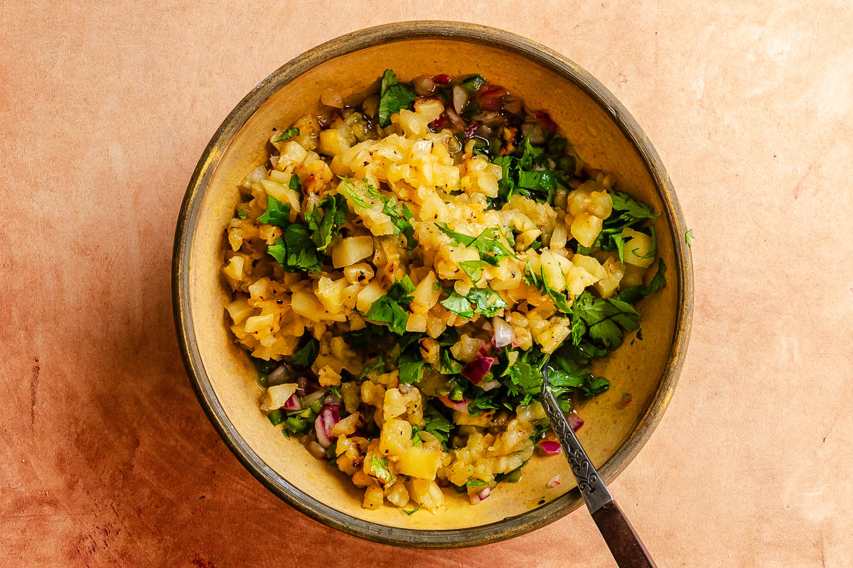 Diced pinapple, minced serrano, red onion and garlic in a small yellow bowl.