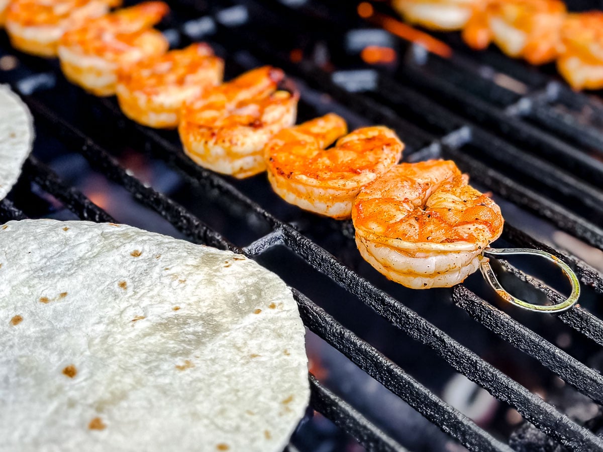 Shrimp skewers grilling on a barbecue, with flames visible underneath the metal grate.