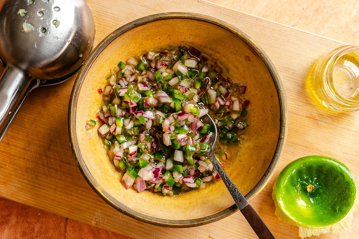 Minced serrano, red onion and garlic mixed together in a small yellow bowl.