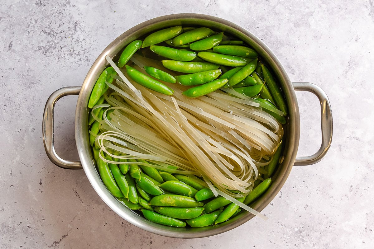 Rice noodles and snap peas cooking in a pot of water together.