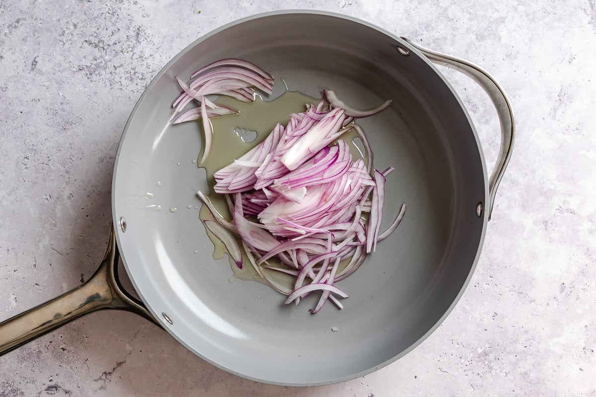 Sliced red onion cooking in a large nonstick skillet.