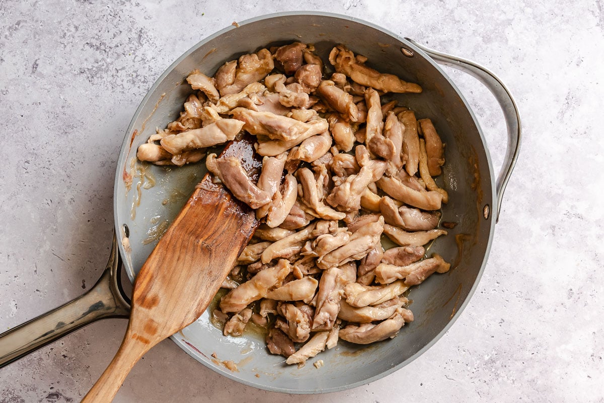 Cooked sliced chicken thighs in a large saute pan.