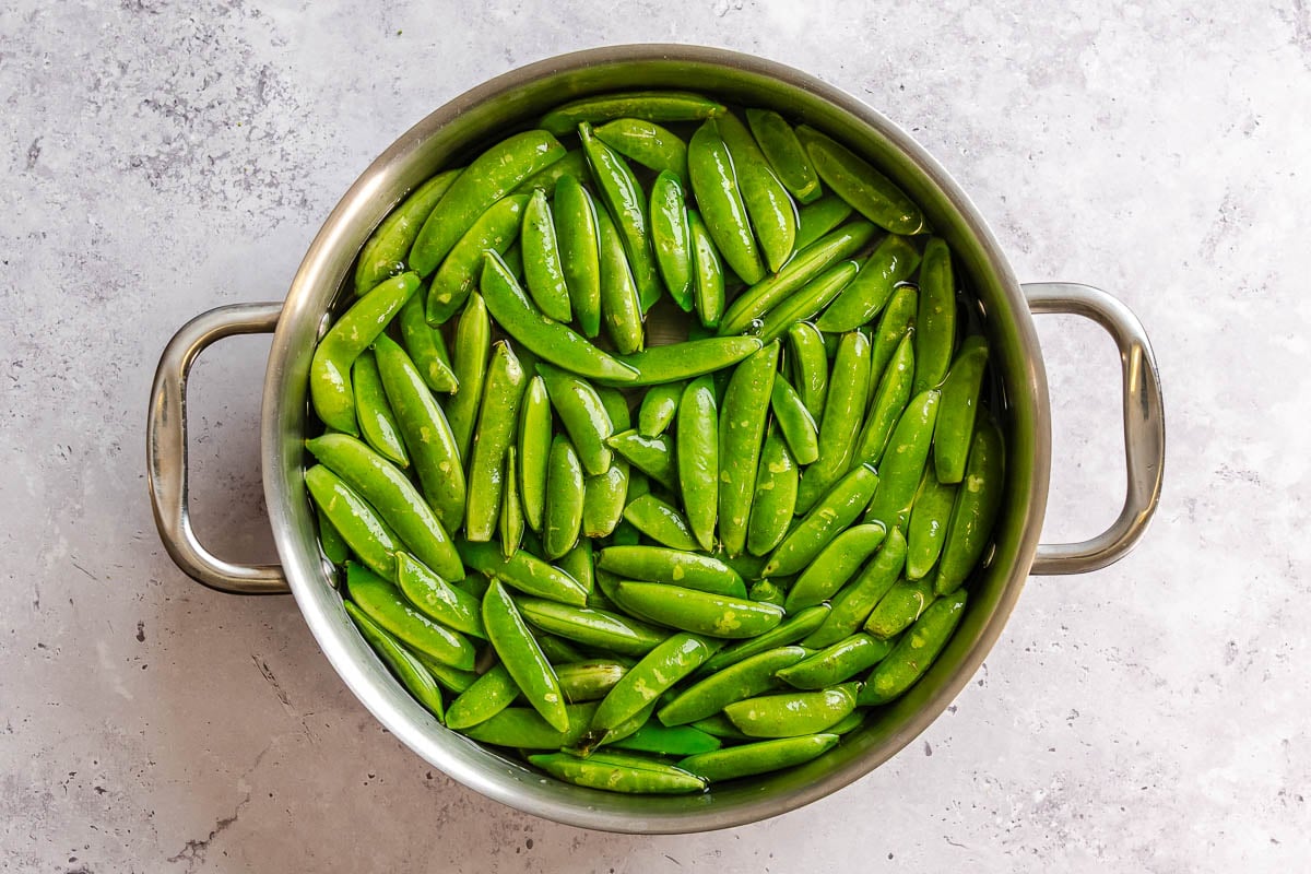 Snap peas blanching in a large saucepan.