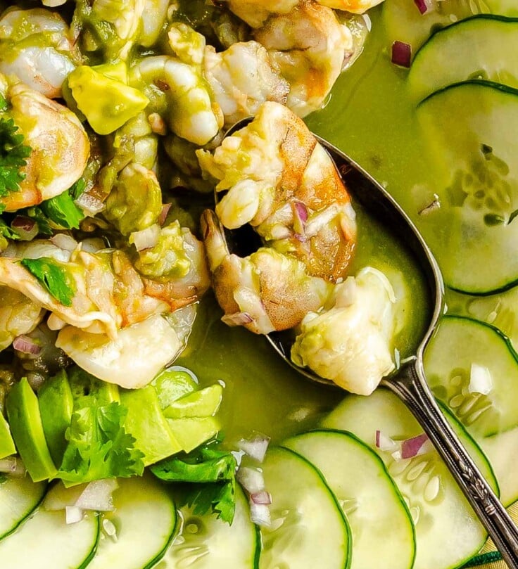 Silver spoon scooping up shrimp and scallop aguachile in a vibrant green sauce topped with avocado.