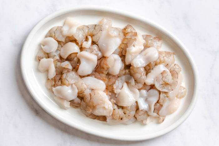Raw, peeled, and deveined shrimp and slices scallops arranged on a white oval plate, viewed from above.