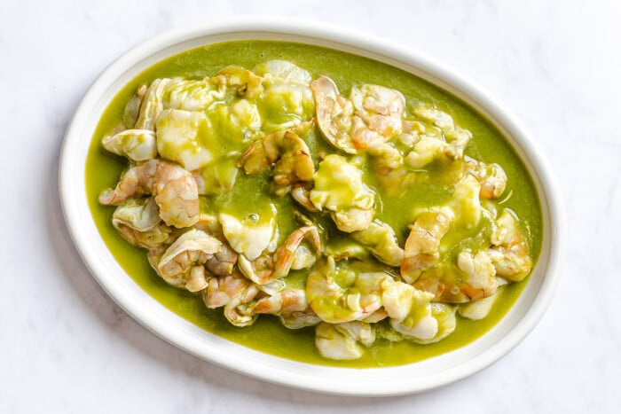 Sliced raw shrimp and scallops in a vibrant green sauce on a large oval platter.