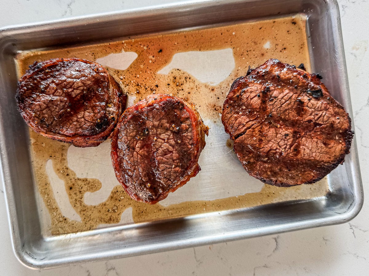 Grilled bacon wrapped steaks on a sheetpan.