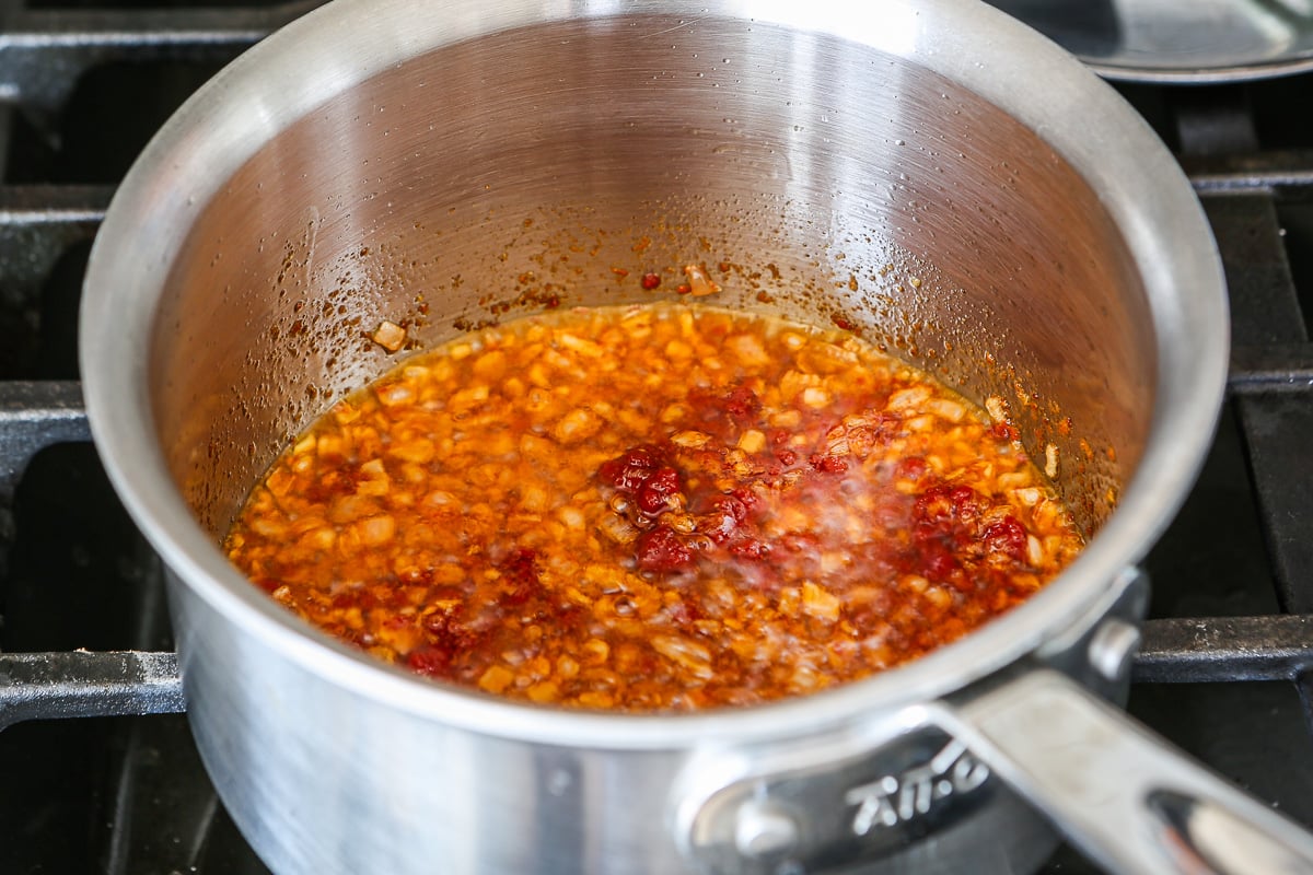 Diced shallots and tomato pastes cooking in a saucepan.