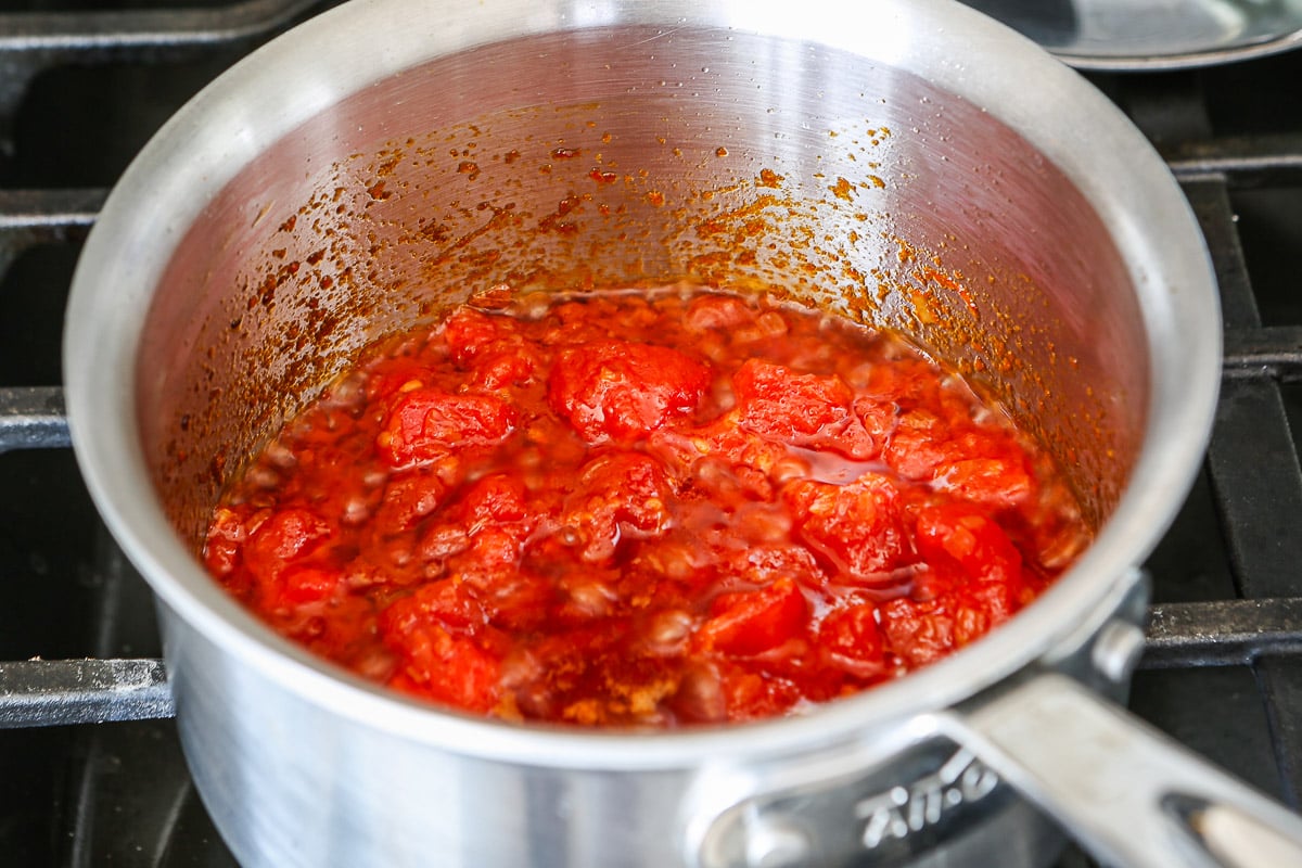 Peeled tomatoes cooking in oil and shallots in a saucepan.