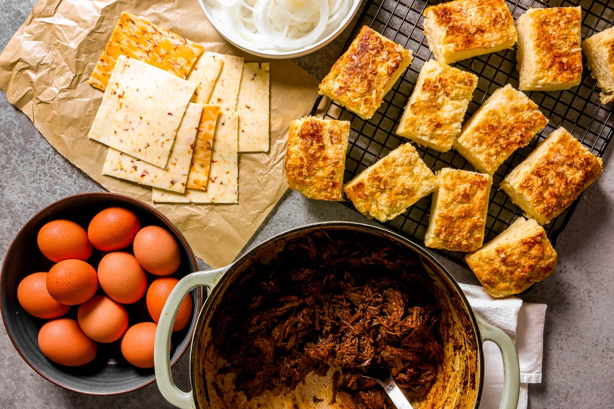 Biscuits, deli sliced pepper jack cheese, sliced onion, eggs, and shredded beef set out on a counter.