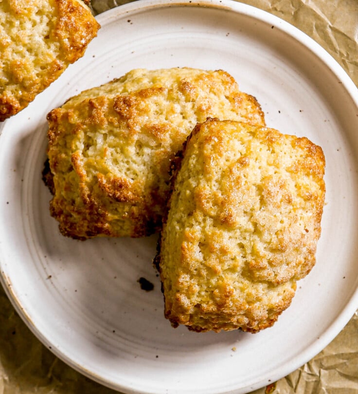 Two golden-brown scones on a white plate, set on crumpled brown parchment paper.