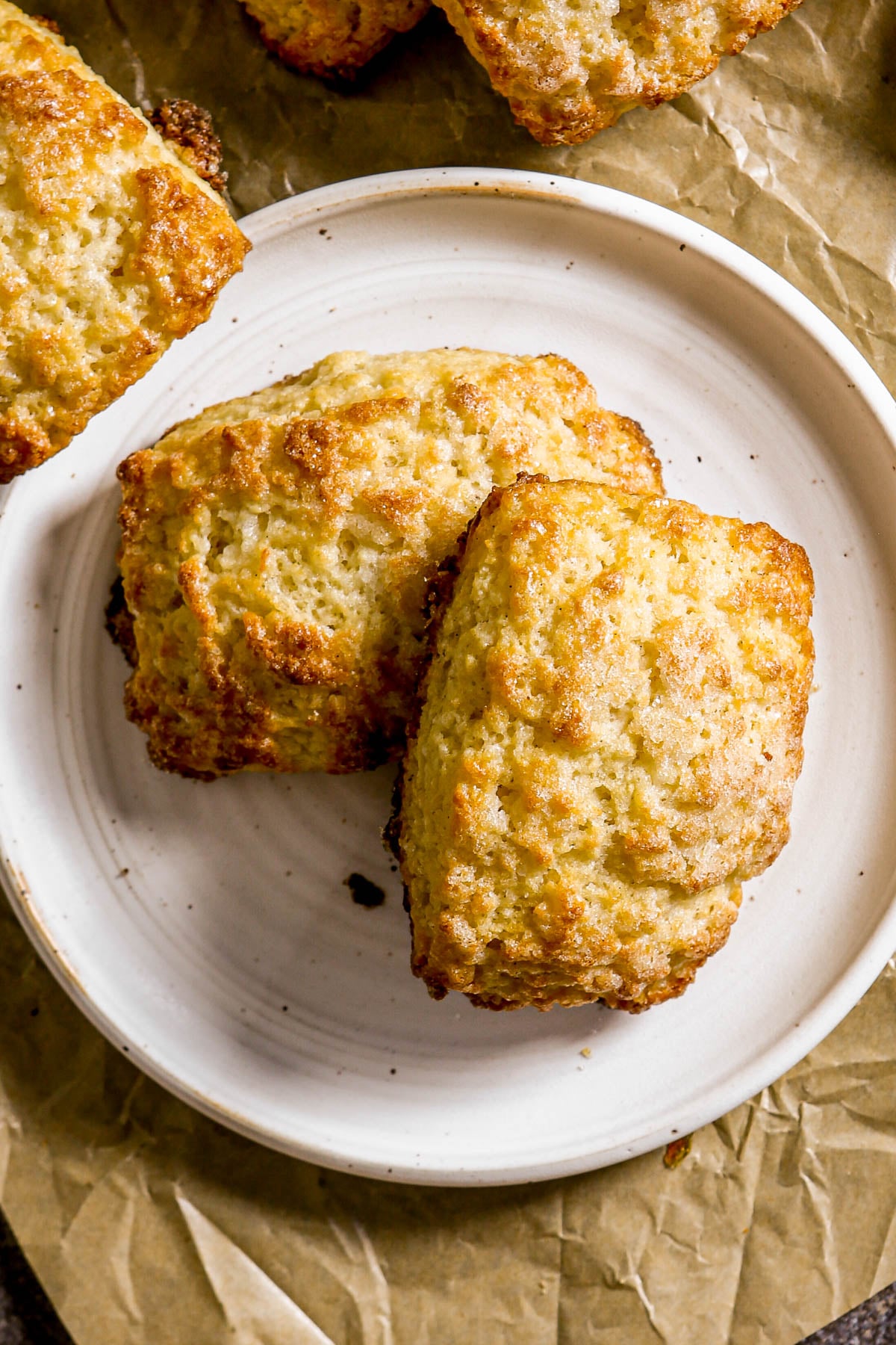 Two golden-brown scones on a white plate, set on crumpled brown parchment paper.