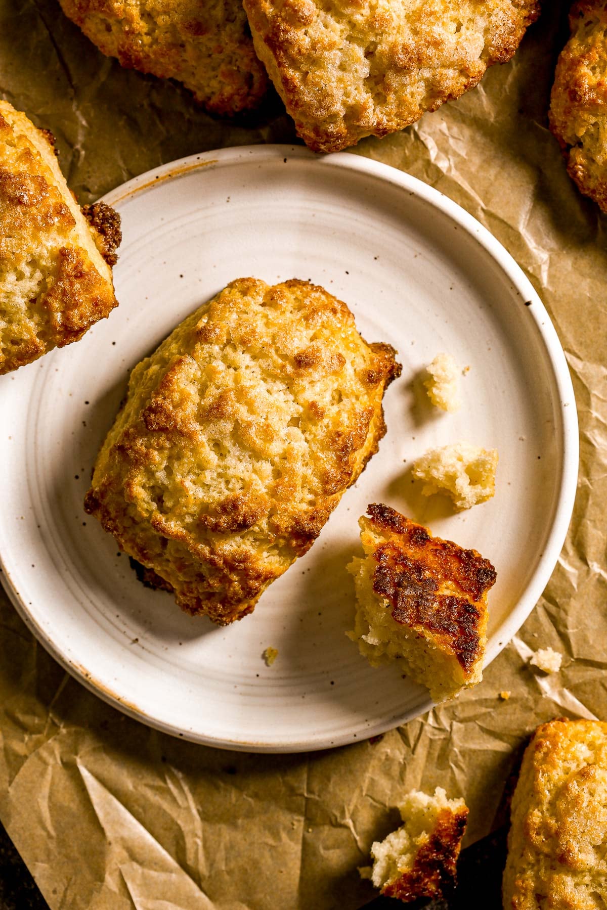 Two golden-brown scones on a white plate, set on crumpled brown parchment paper.
