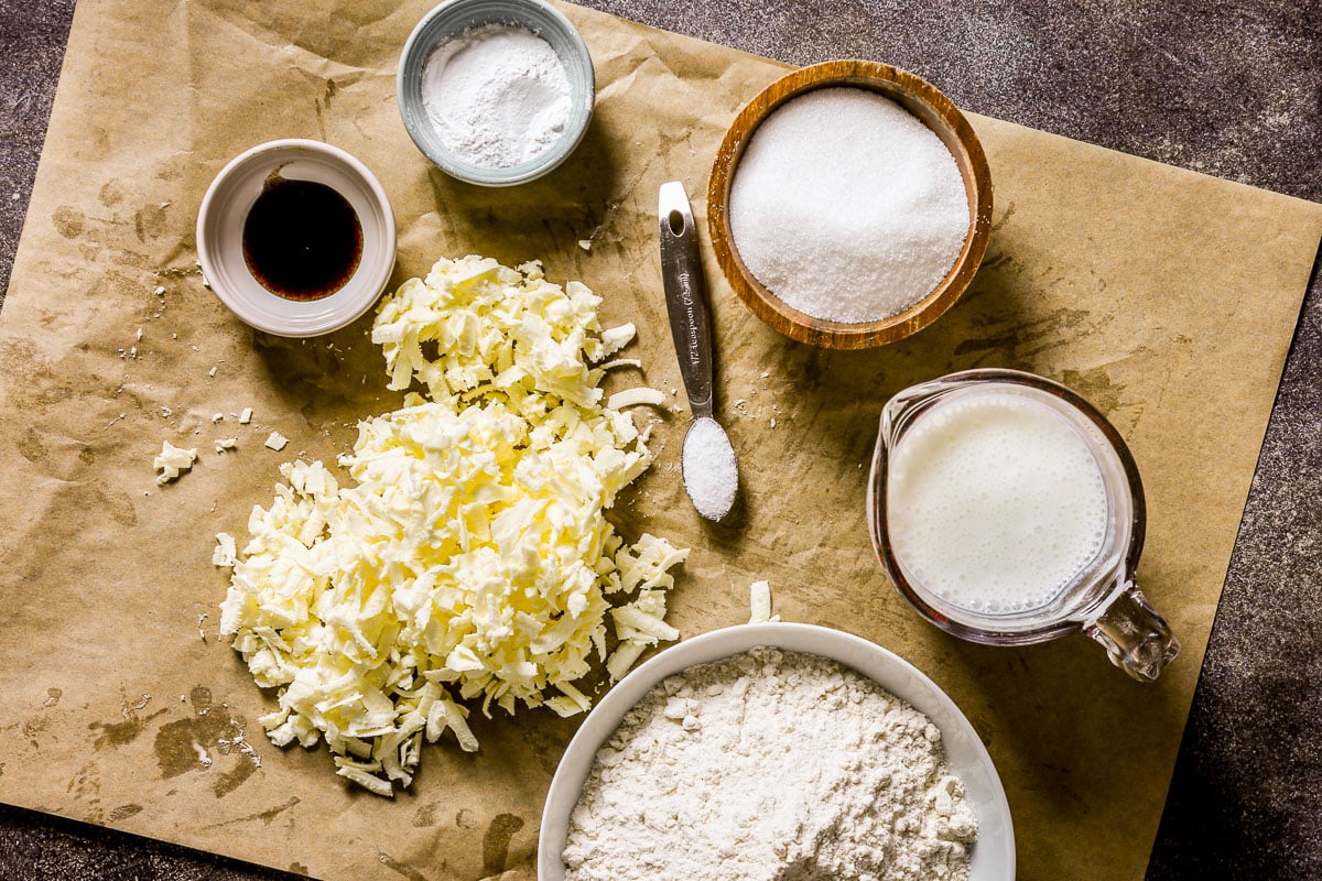 Baking ingredients on parchment: grated butter, flour, sugar, vanilla, baking powder, salt, and buttermilk.