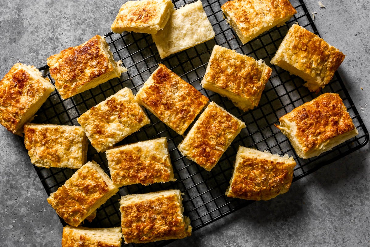 Golden, square biscuits cooling on a black wire rack set on a gray countertop.