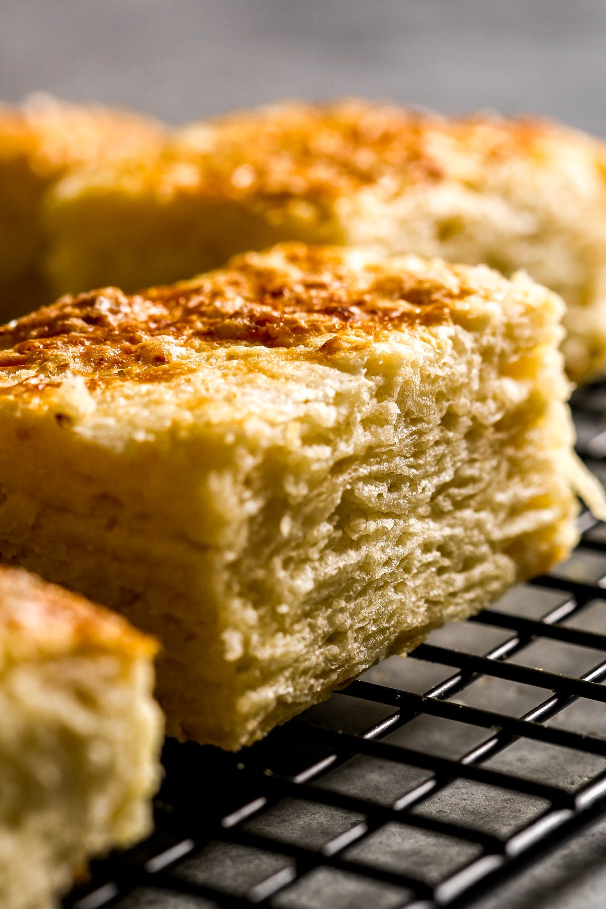 Close-up of golden, buttermilk biscuits cooling on a black wire rack.