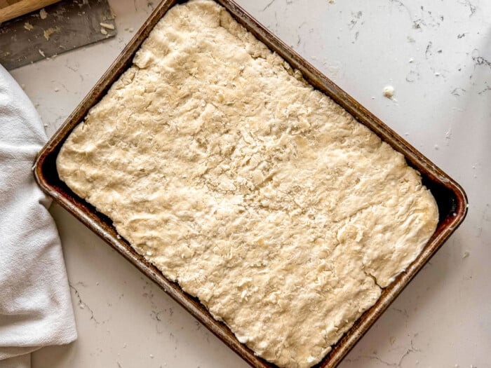 Biscuit dough pressed into a sheet pan set on a gray counter.