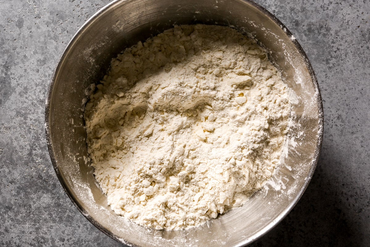 Large metal bowl of flour tossed with shredded butter.