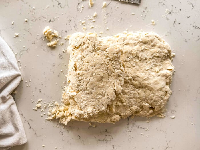 Rough biscuit dough folded on a floured countertop next to a white cloth.