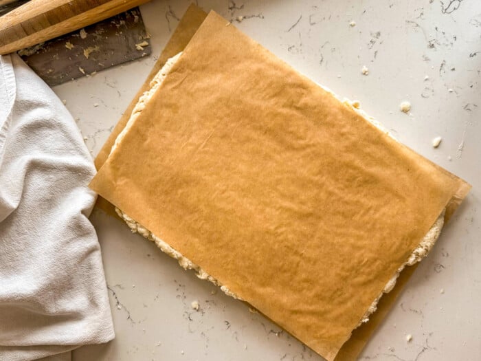 Square of biscuit dough rolled out between sheets of brown parchment paper.