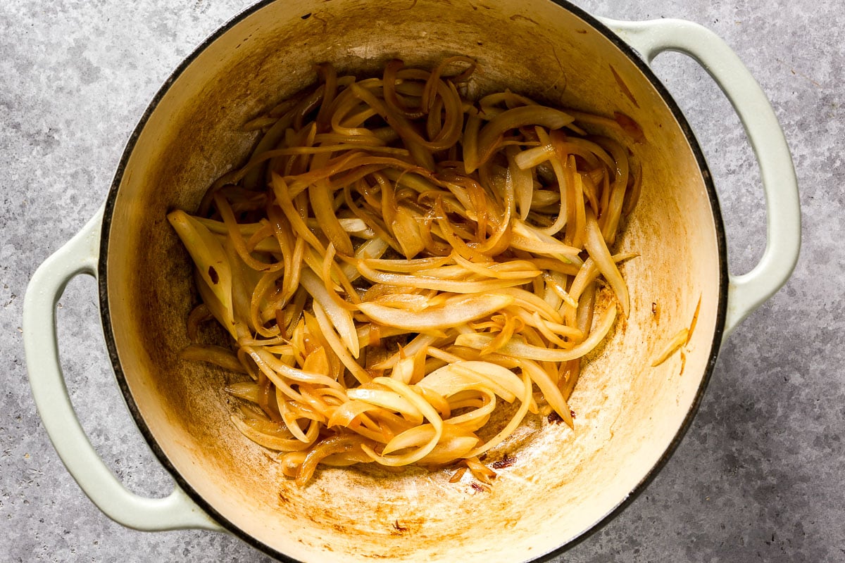 Sliced onions caramelizing in a large cream-colored pot on a gray countertop.