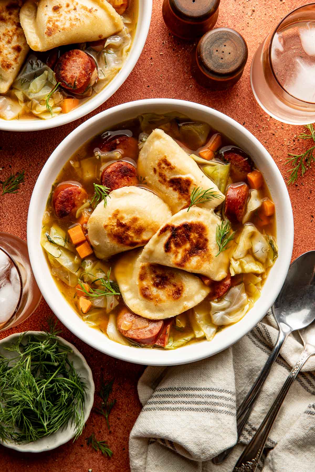 Bowl of sausage cabbage soup with sliced browned smoked sausage, cabbage, and seared pierogi, garnished with fresh dill.