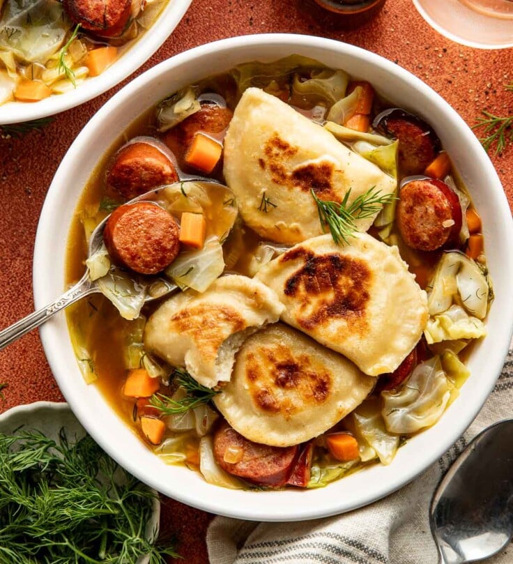 Bowl of soup made with sliced polish sausage, cabbage, carrots, and pierogi topped with fresh dill.