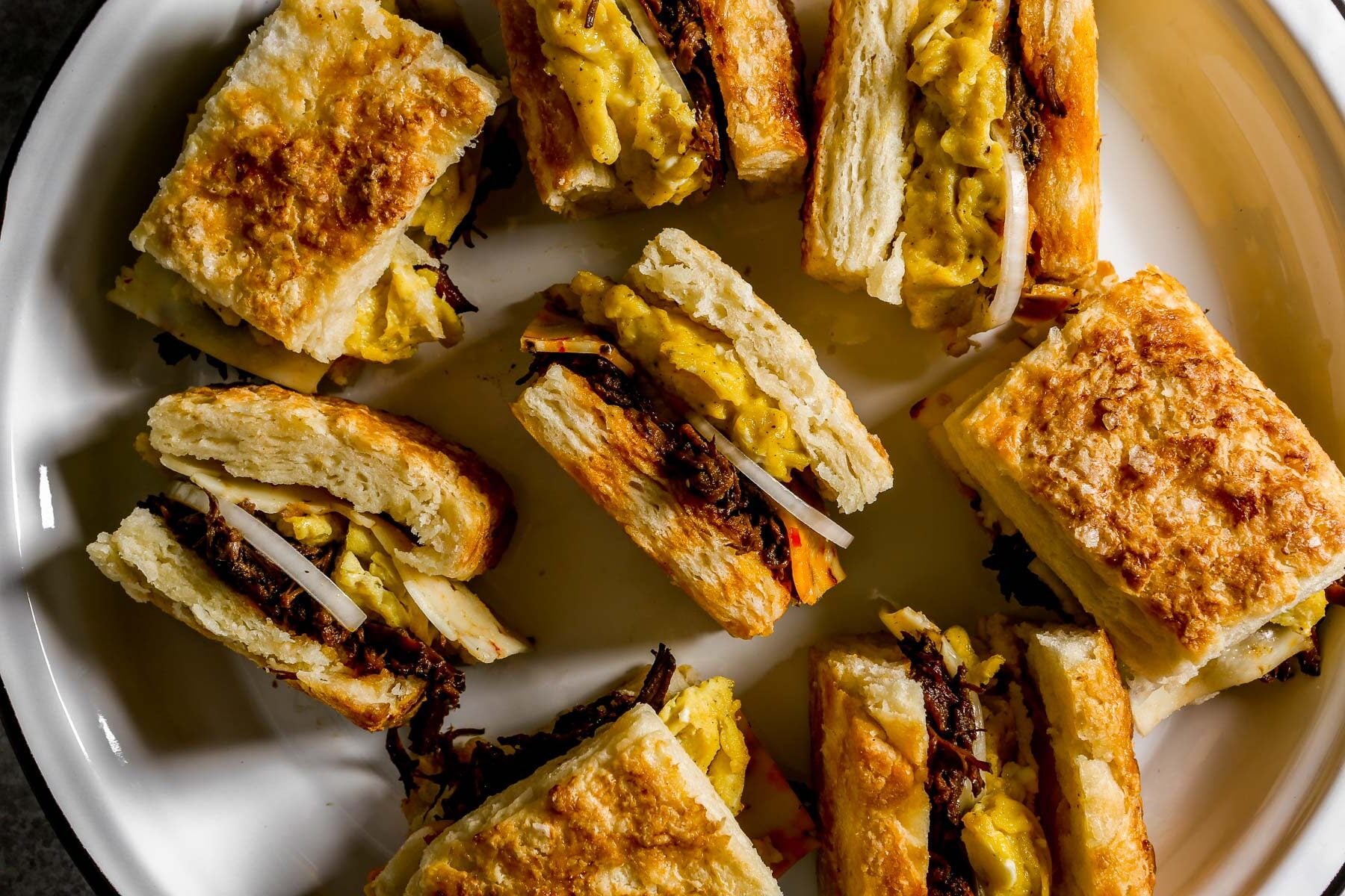 Biscuits filled with scrambled eggs, shredded beef, cheese and sliced onion arranged on a white plate.