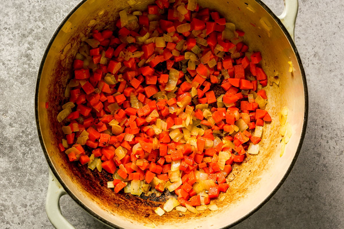 Diced carrots and onions sautéing in a Dutch oven.