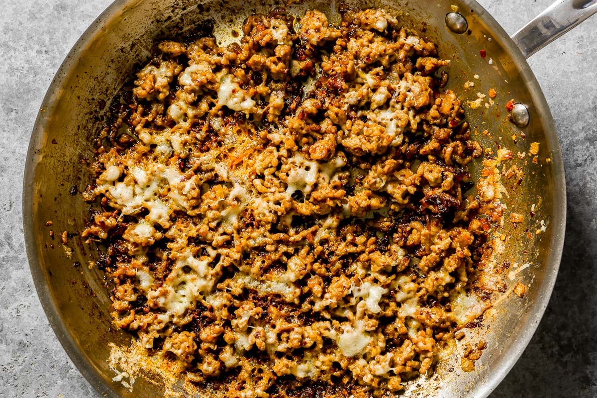 Cooked ground pork with melted cheese in a stainless steel skillet.