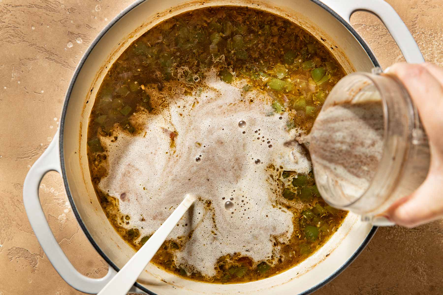Pureed soup being poured into a pot of black bean soup.