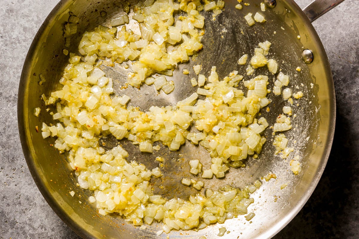 Diced onions sautéing in a stainless steel skillet.