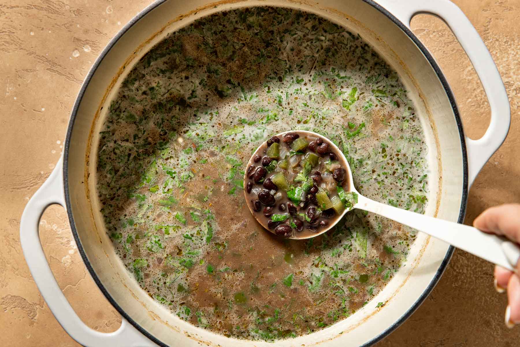 A ladle lifting black bean soup from a large pot.