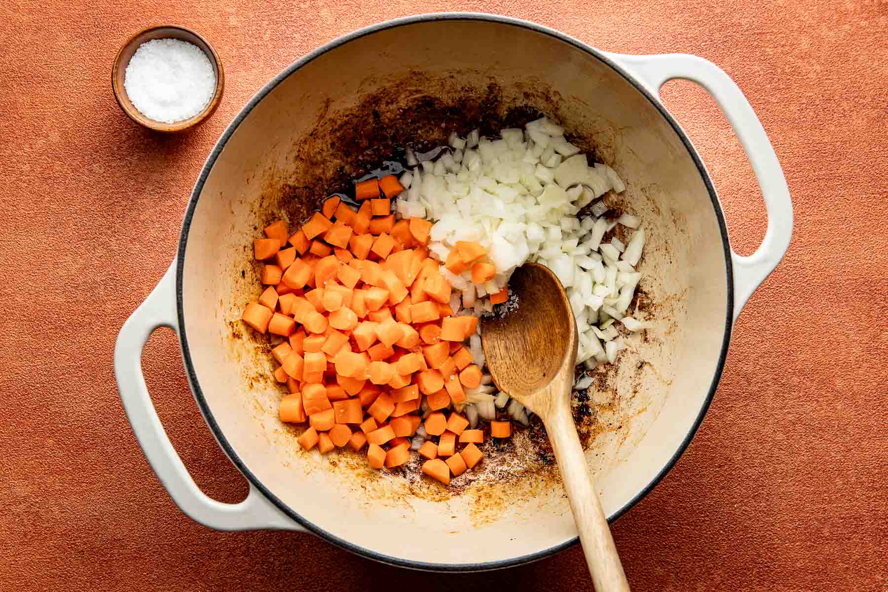 Diced carrots and onions cooking in drippings from browning sausage in a large pot.