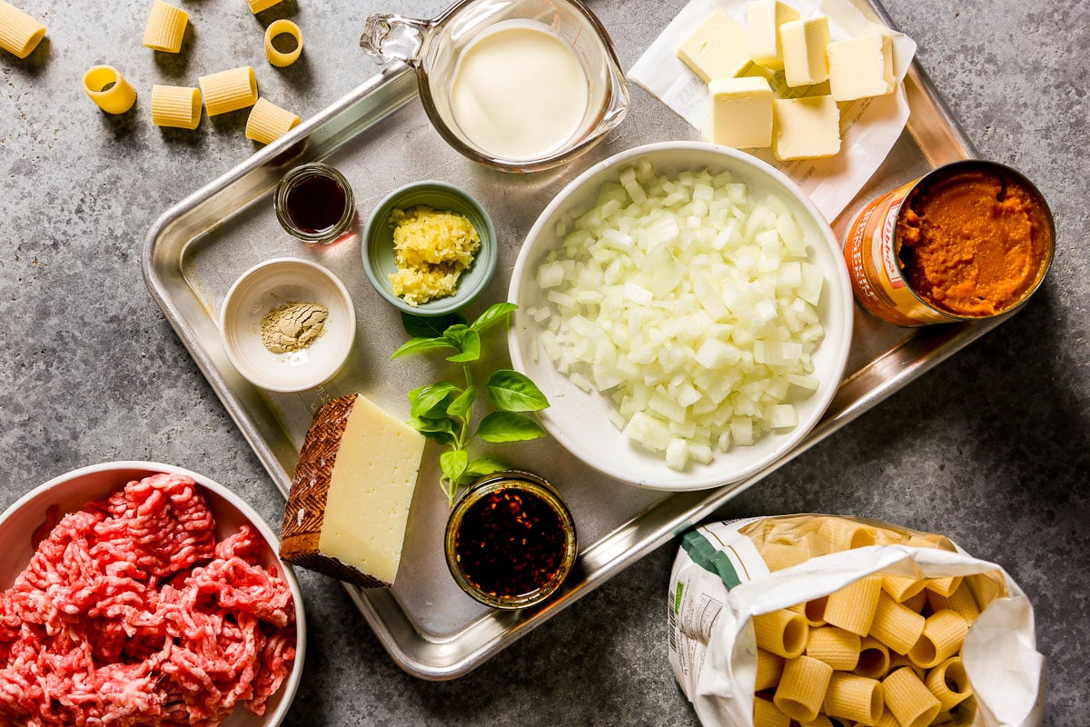 Ingredients for pumpkin pasta on a large metal tray including ground pork, pasta, chopped onions, butter, cream, a can of pumpkin, basil, cheese, vinegar, and garlic.
