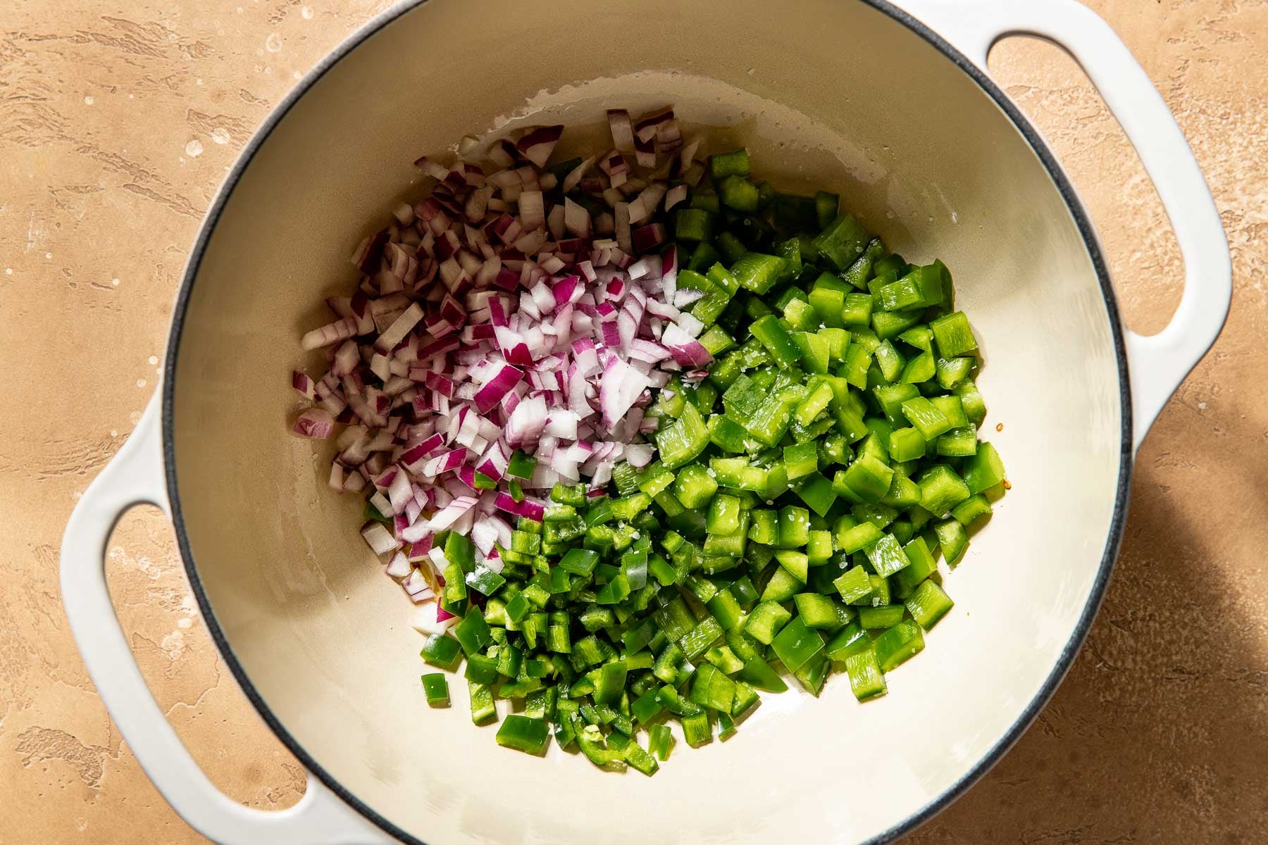 Diced red onion and green bell pepper cooking in a white pot.