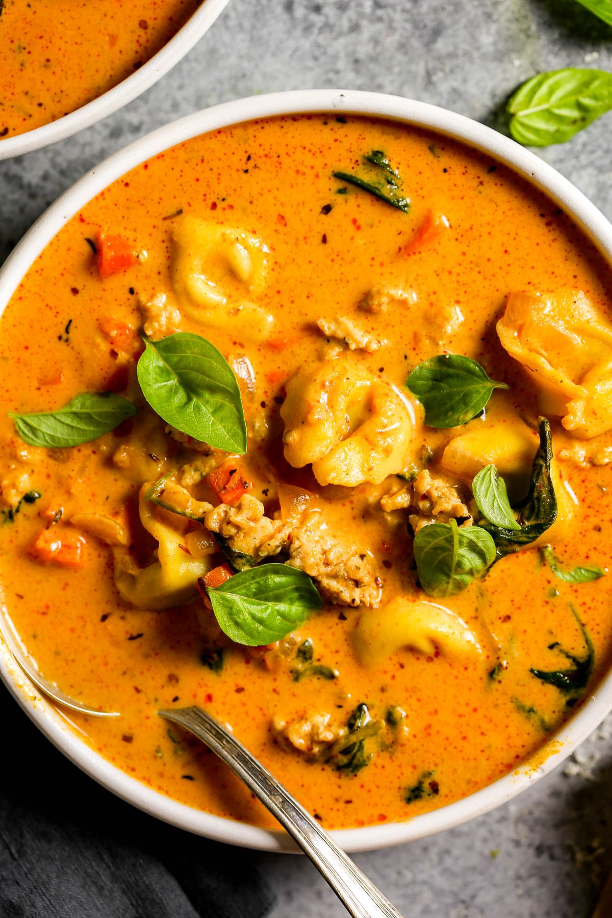 Creamy tomato soup with tortellini, ground chicken, and fresh basil leaves in a white bowl.
