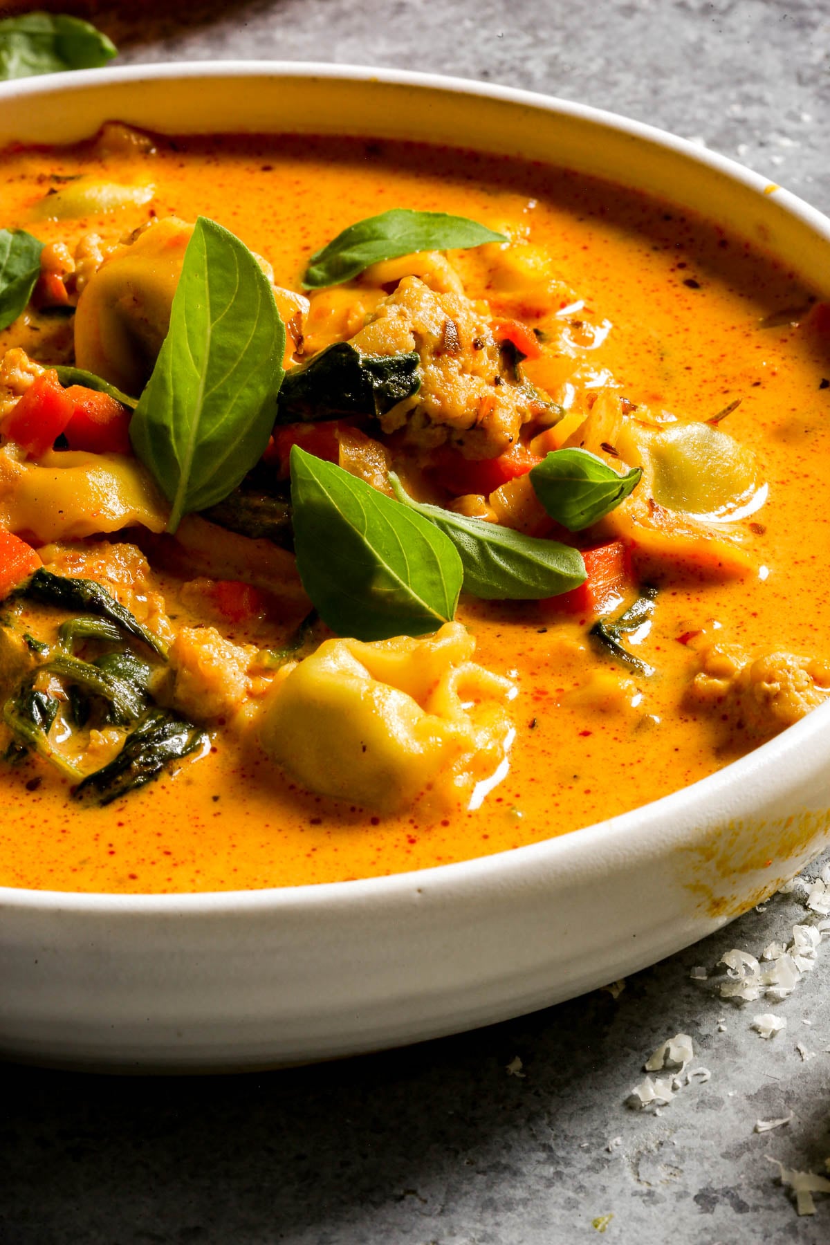 Creamy tomato soup with tortellini, greens, and chicken, topped with fresh basil, in a white bowl.